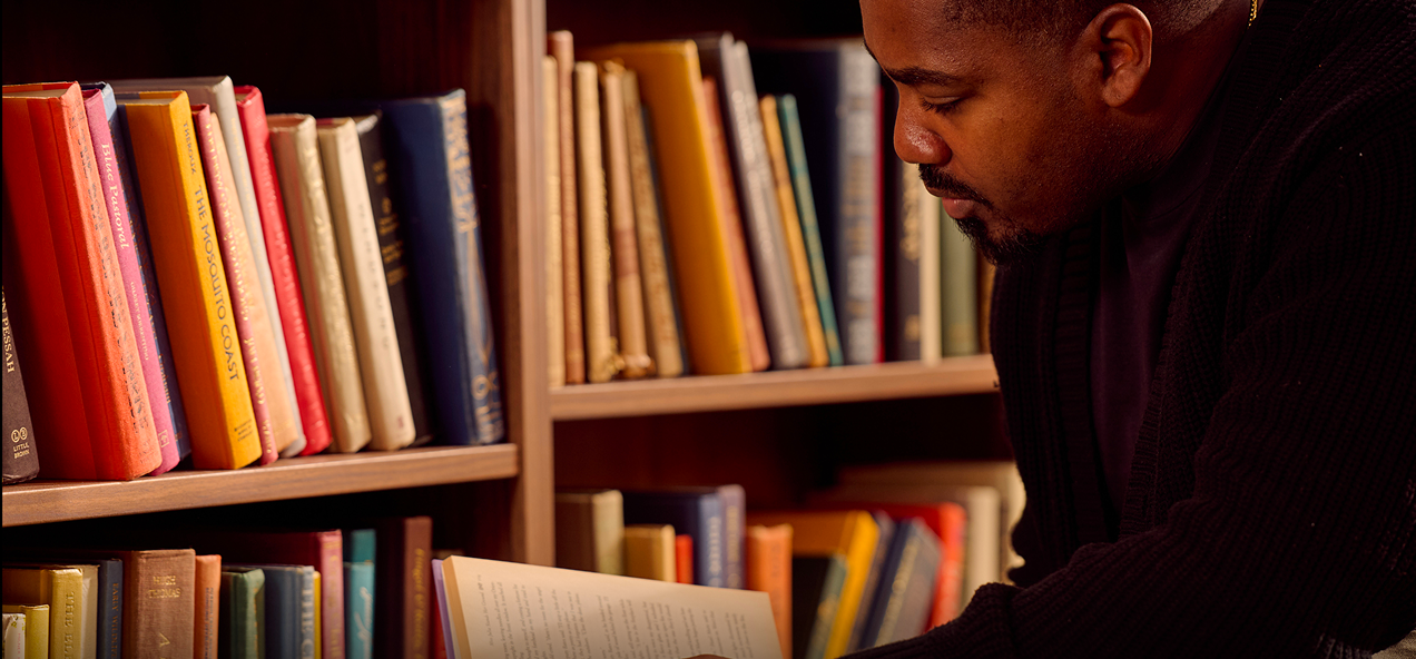 Man looking down reading a book in a library