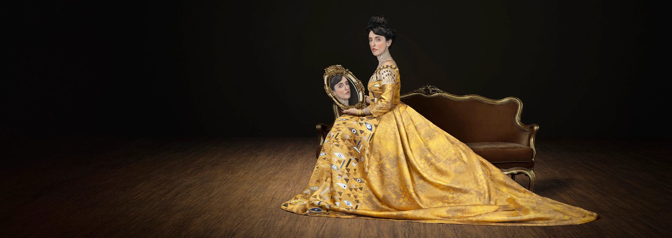 Campaign imagery of seated model in gold dress